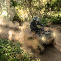 A man rides a camoflauge 2023 Kawasaki Brute Force® ATV through the woods